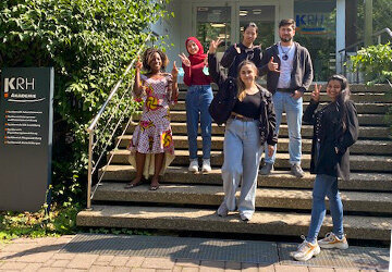 Sechs Absolventinnen und Absolventen des Deutschkurses an der KRH Akademie auf einer Treppe draußen.